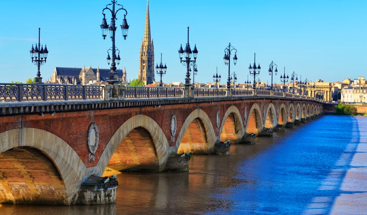 Bridge with lamps and spire of cathedral in distance in Bordeaux