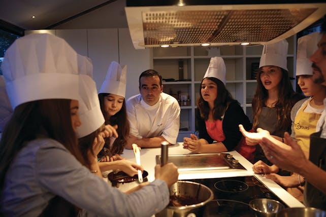 Group of ladies in chefs hats with chef, looking at people cooking