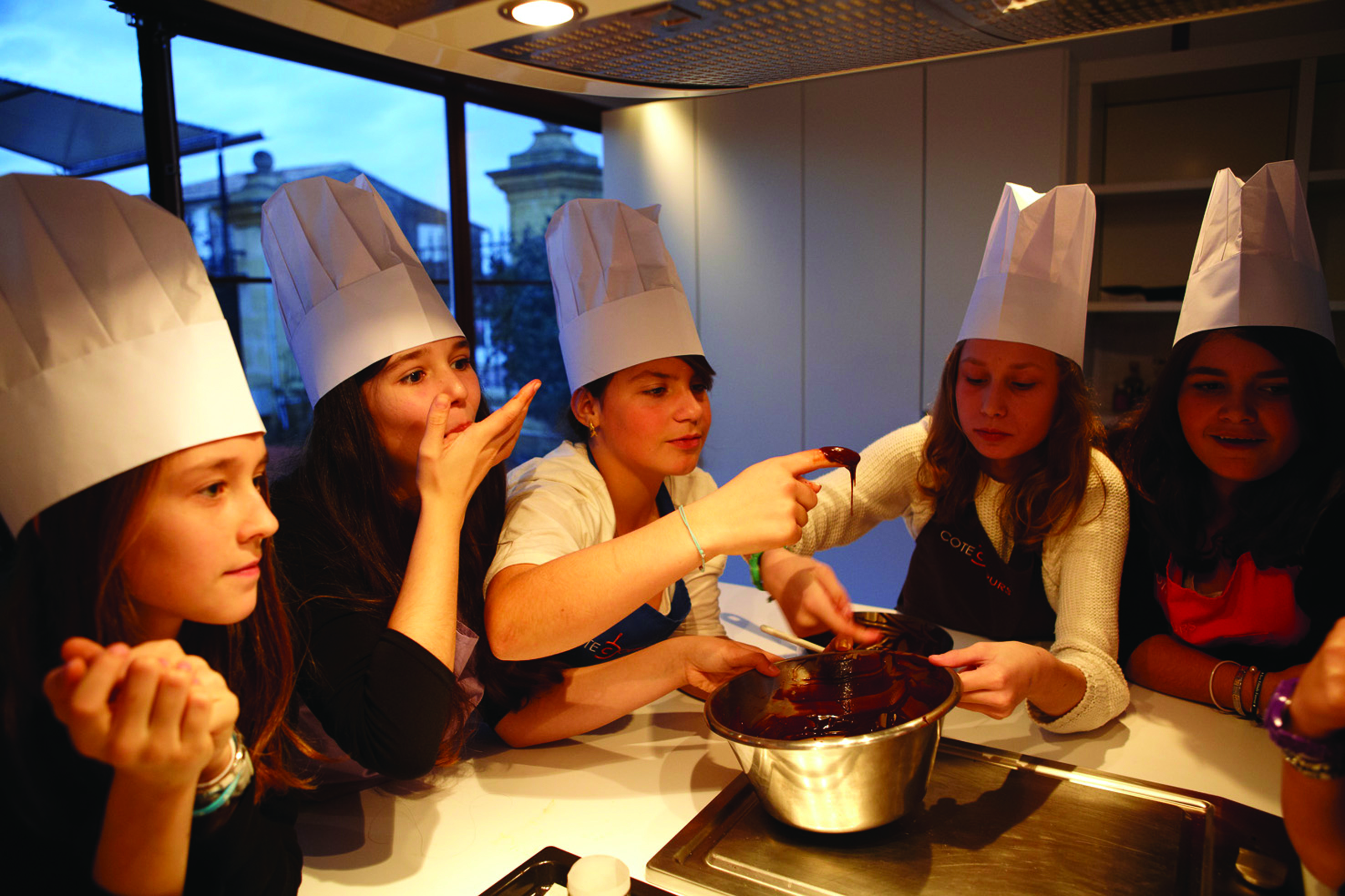 Group of ladies with chefs hats looking at cooking things