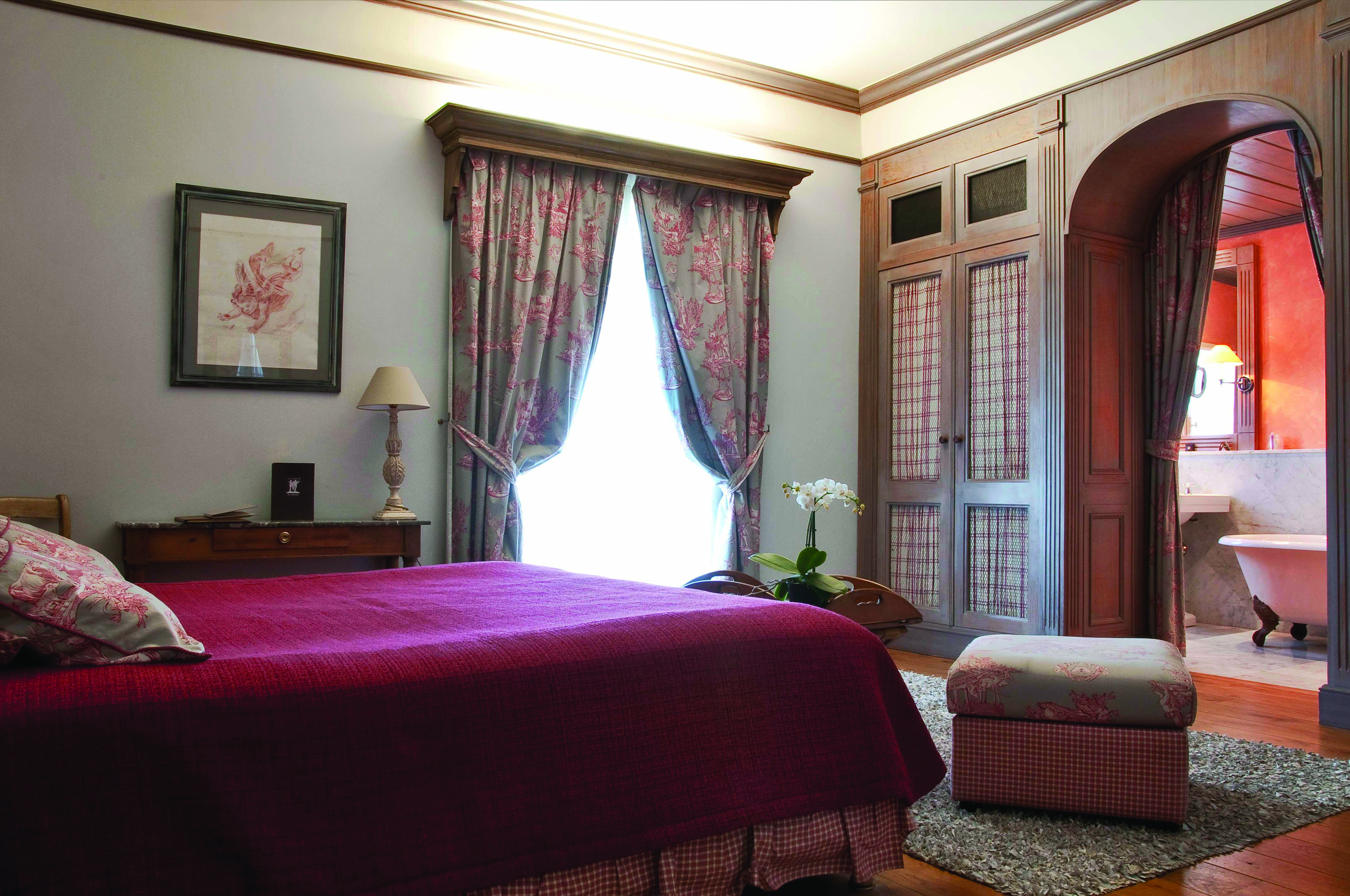 Bedroom at the Les Sources de Caudalie with large double bed, archway leading into bathroom and draping curtains