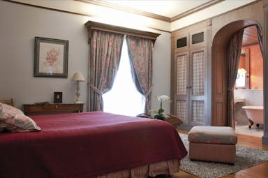 Bedroom at the Les Sources de Caudalie with large double bed, archway leading into bathroom and draping curtains