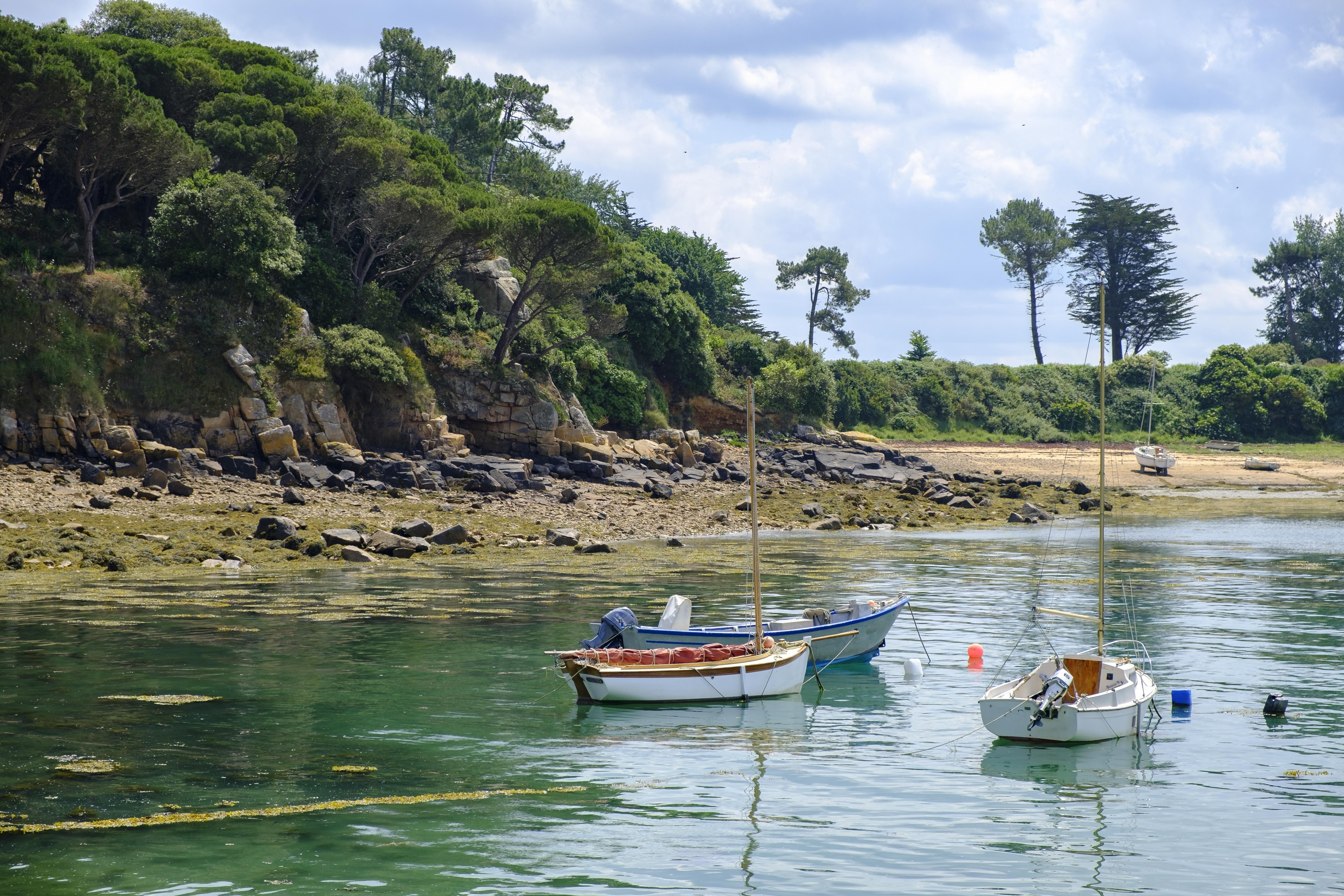 Small boats on calm water on coast with cliffs behind in Brittany