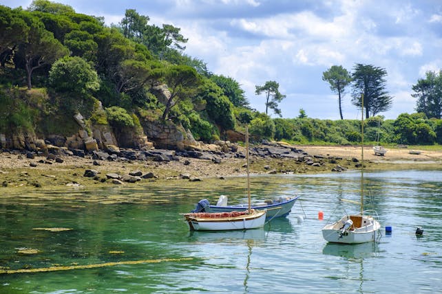 Small boats on calm water on coast with cliffs behind in Brittany