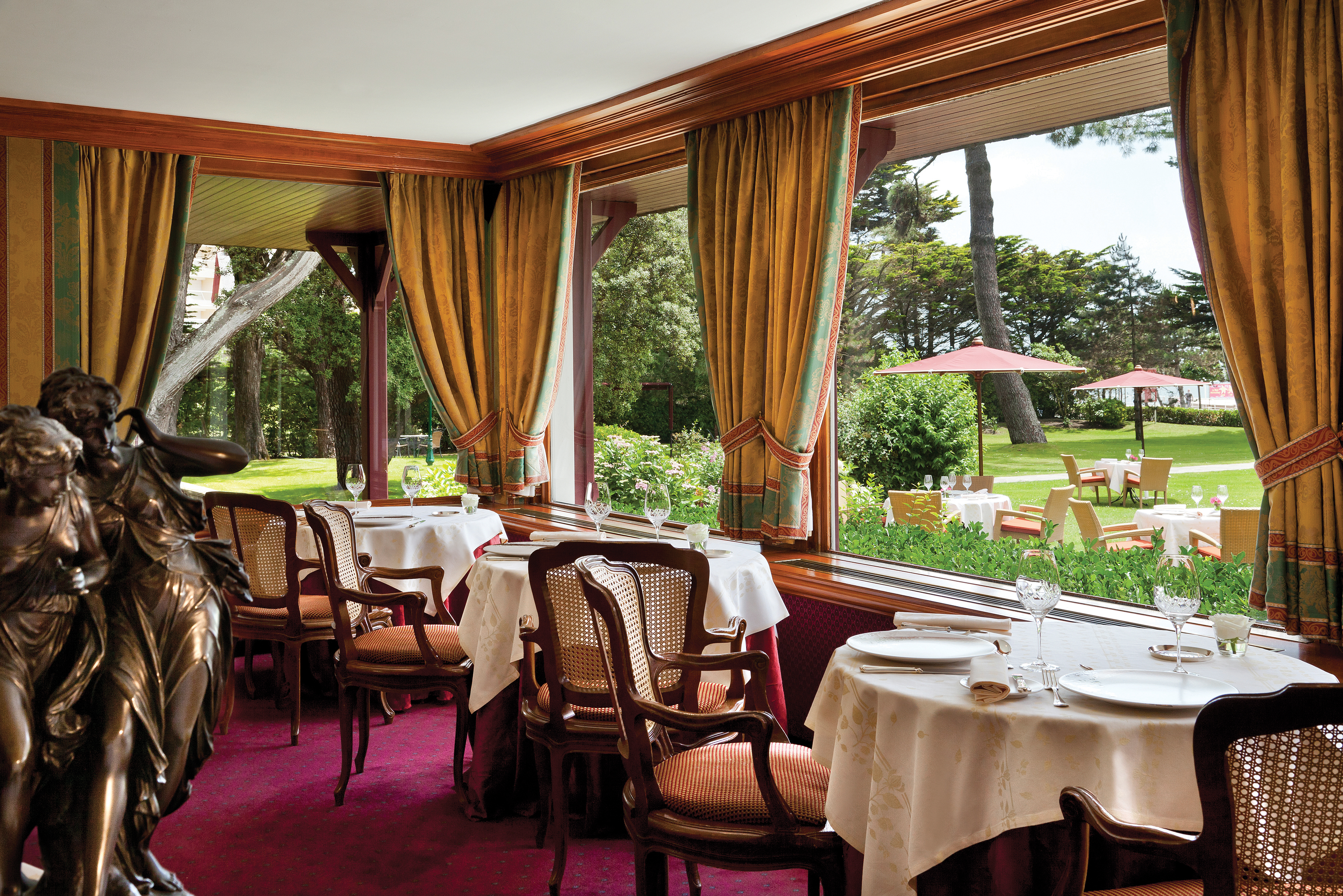Restaurant with tables and chairs set out inside near to windows with views over the gardens