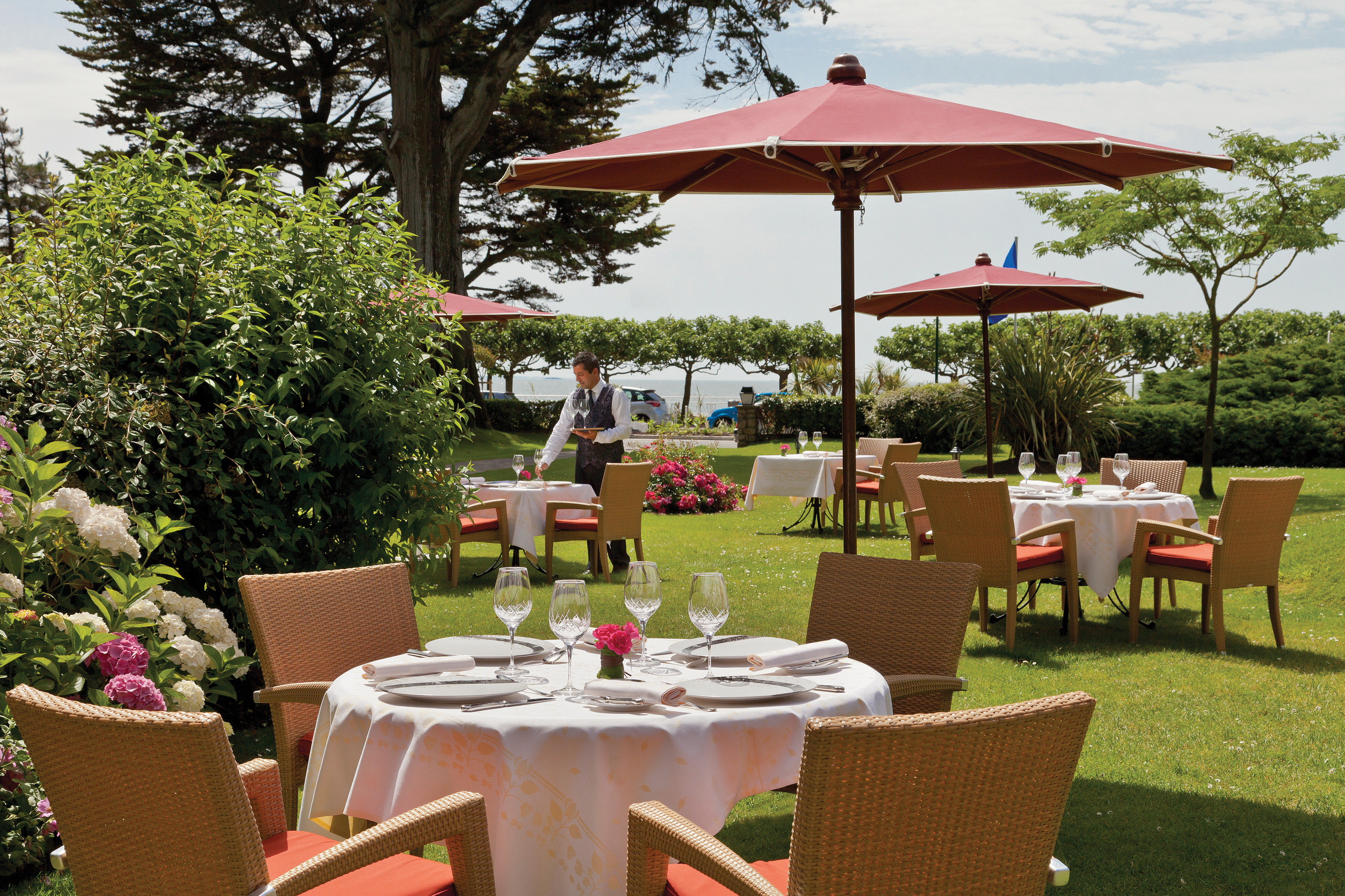 Outdoor dining terrace with tables and umbrellas laid out on the grass amongst trees