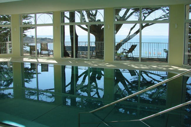 Indoor pool with window pannelled walls leading onto a balcony and looking over the sea