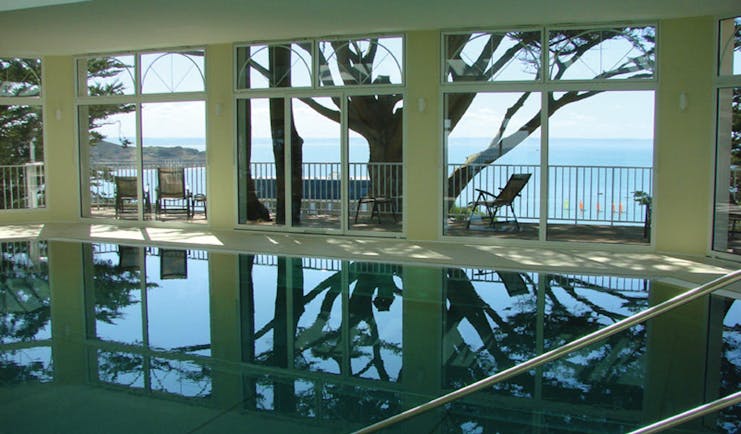Indoor pool with window pannelled walls leading onto a balcony and looking over the sea