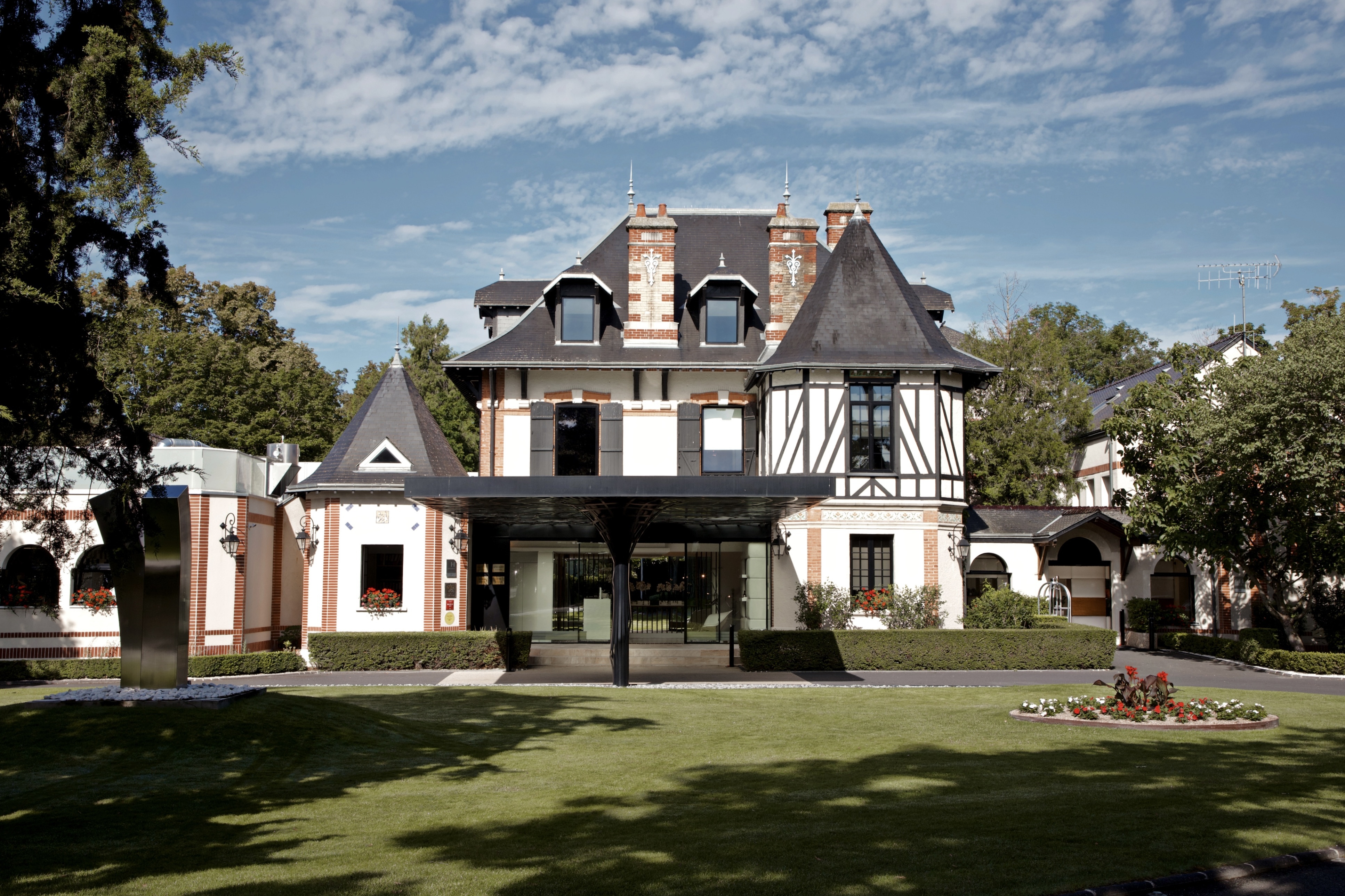 Assiette Champenoise exterior, showing a tudor-style architecture, with plastered white walls and exposed beams, conical, tower-like roofs, and extensive lawns