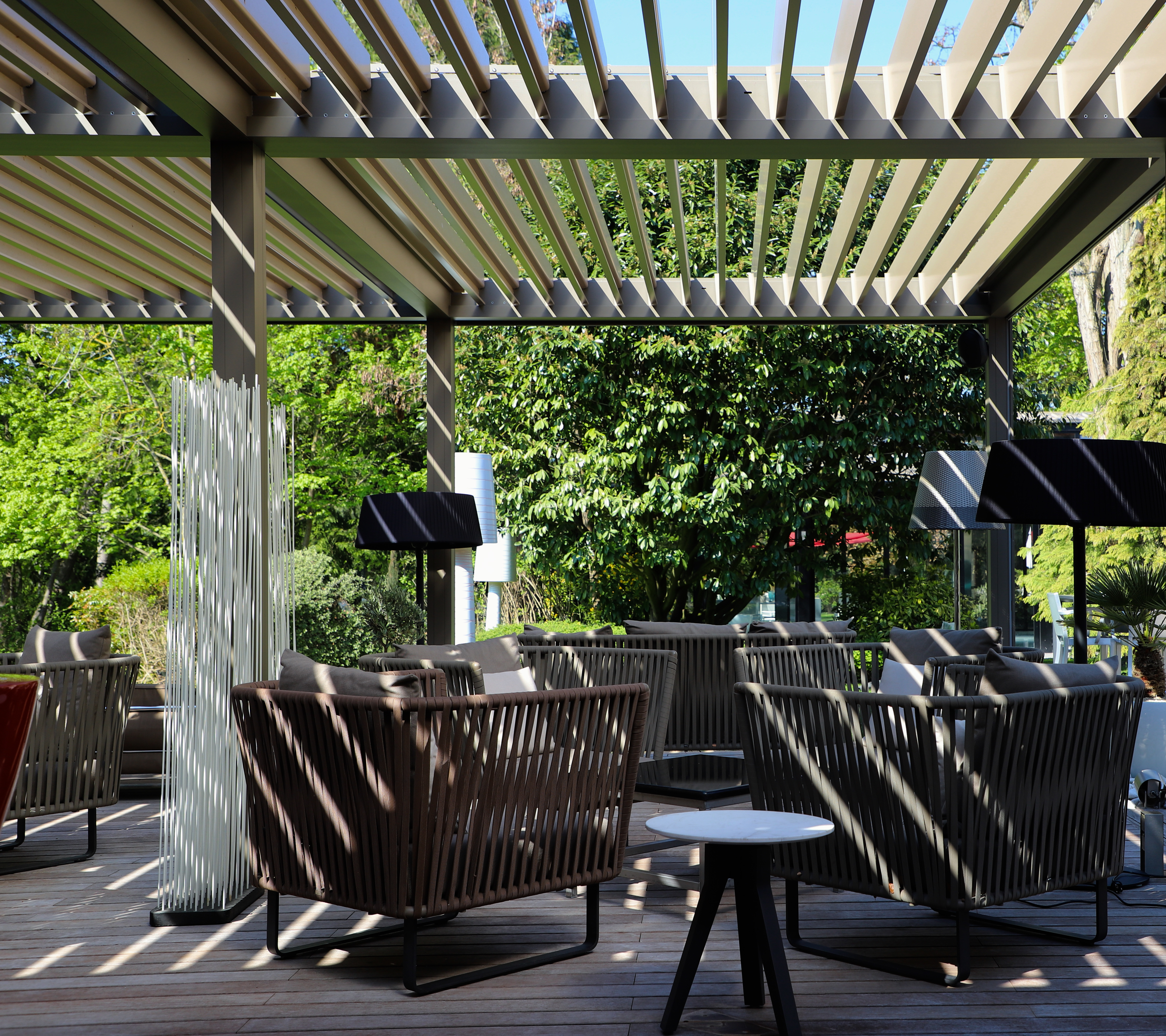 Assiette Champenoise outdoor seating shaded by a simple pergoda, with rattan armchairs, lights for the evening, coffee tables, and views onto the green hotel grounds