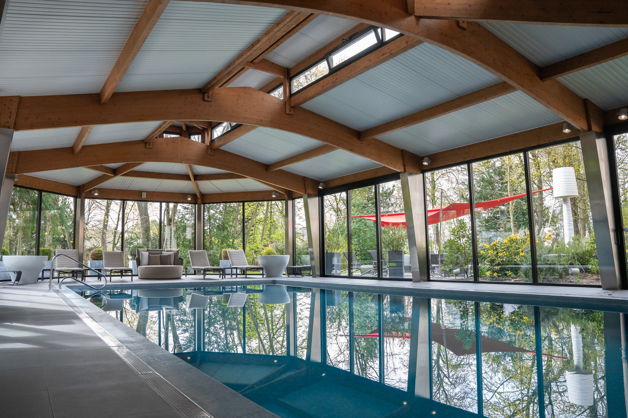 Assiette Champenoise swimming pool with wooden beamed ceiling and floor-to-ceiling windows on all walls looking out into hotel gardens