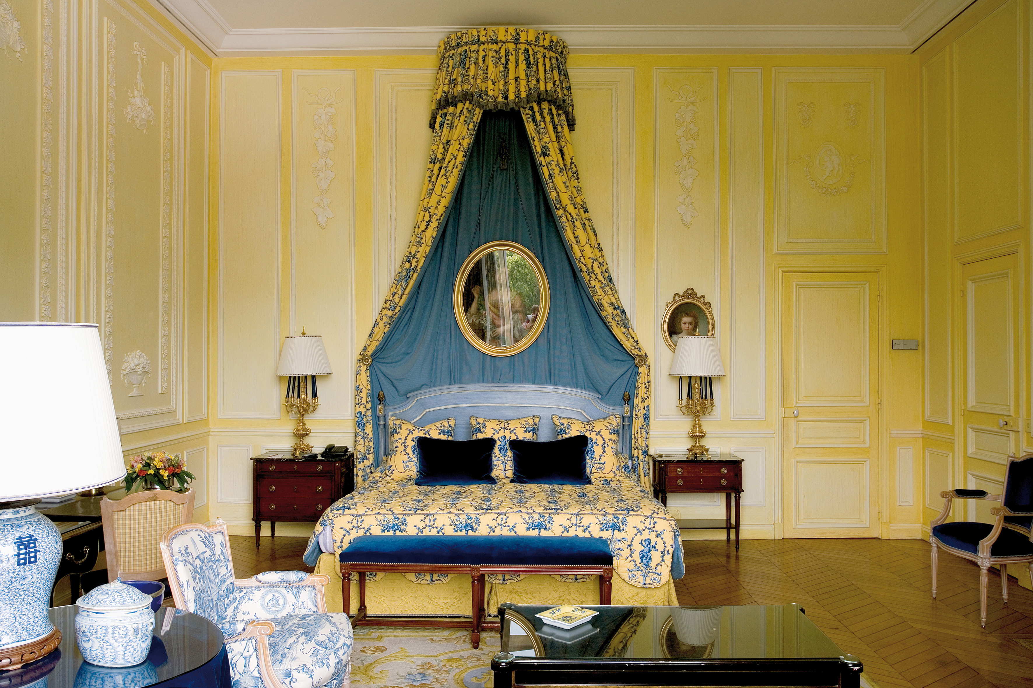 Bedroom with yellow and blue colour scheme, double bed and bed side tables with drapes