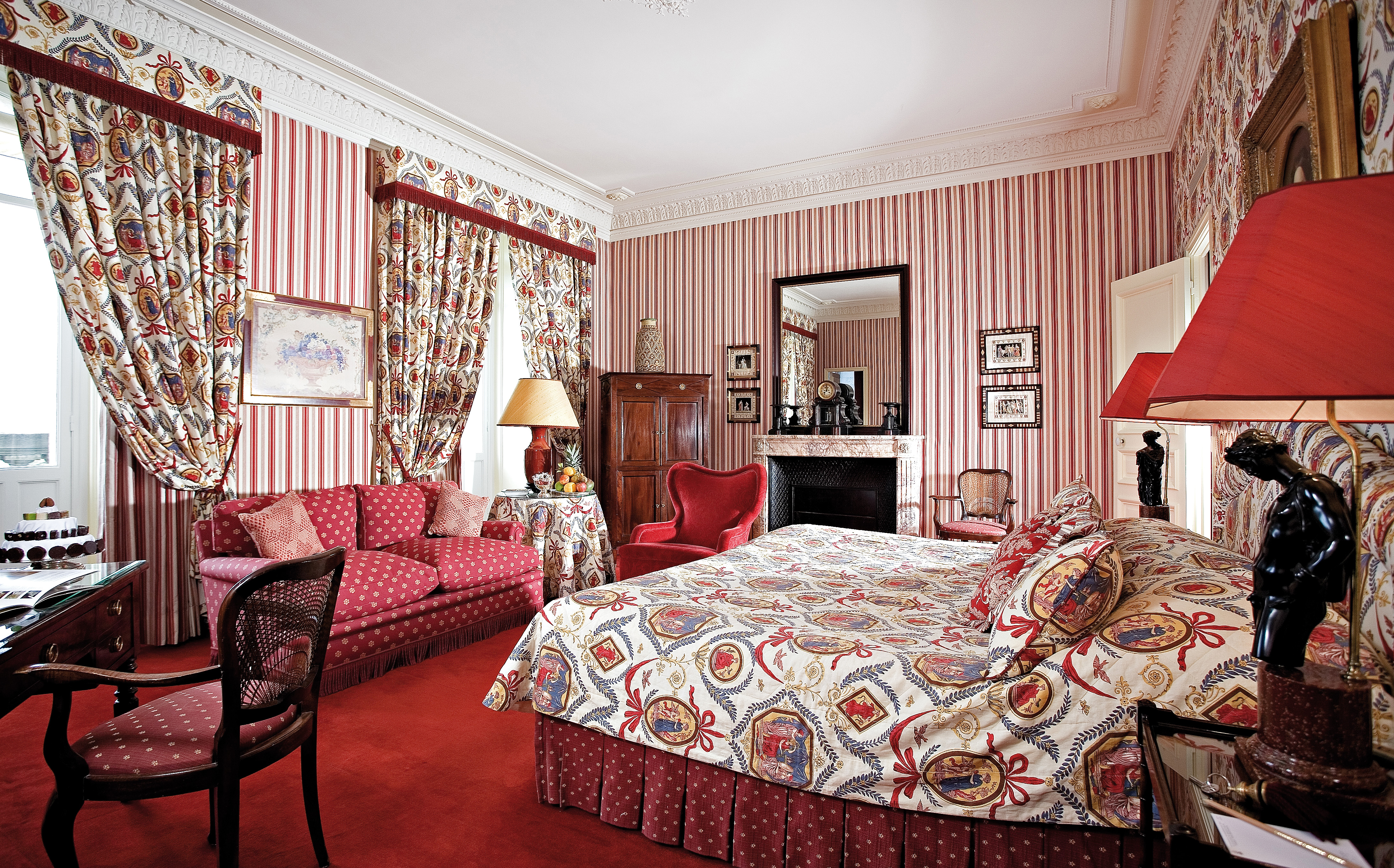 Red colour schemed bedroom with draping curtains, large double bed and sofas