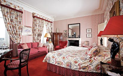 Red colour schemed bedroom with draping curtains, large double bed and sofas