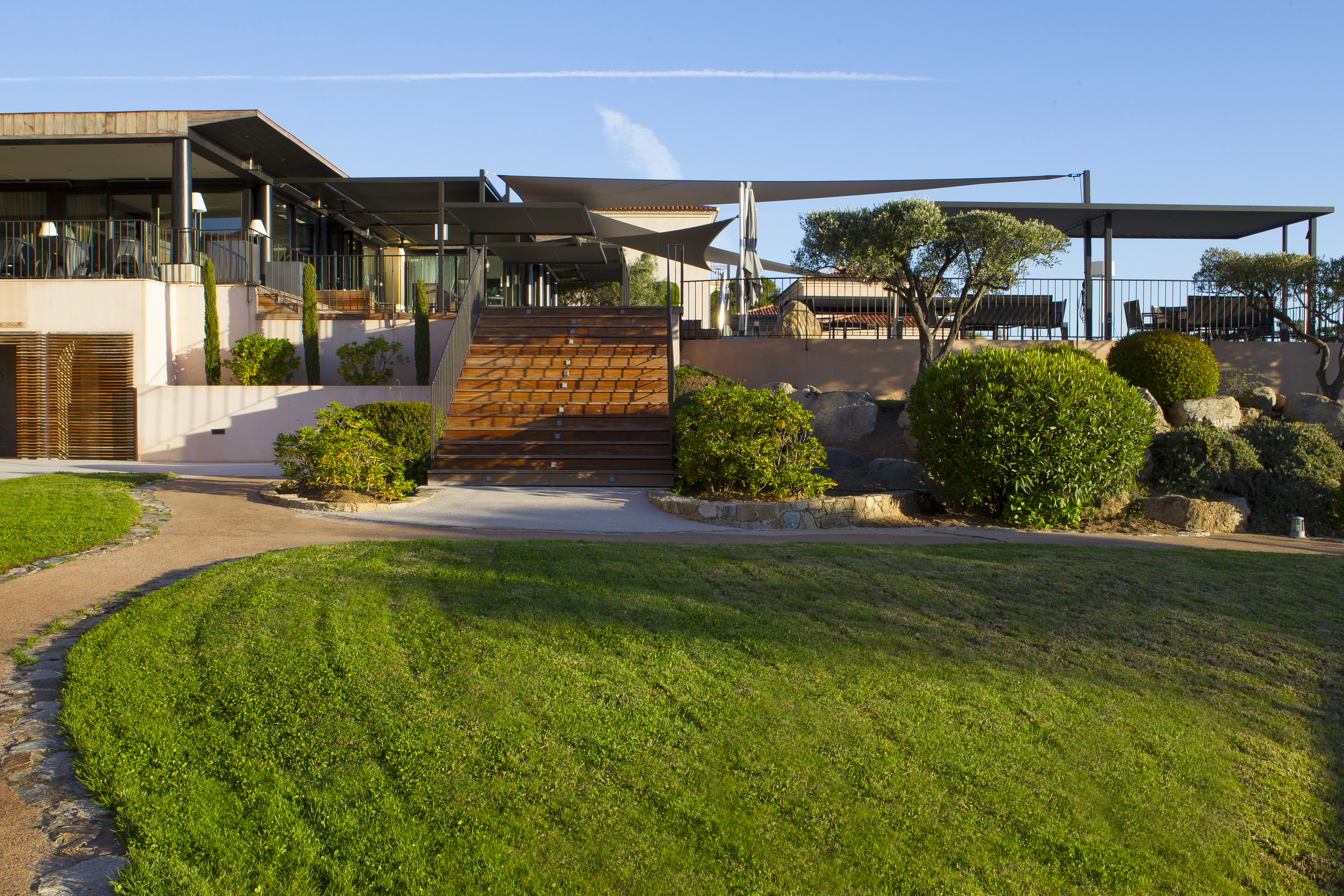 Gardens with green grassy lawn, bushes and steps leading up to a patio area