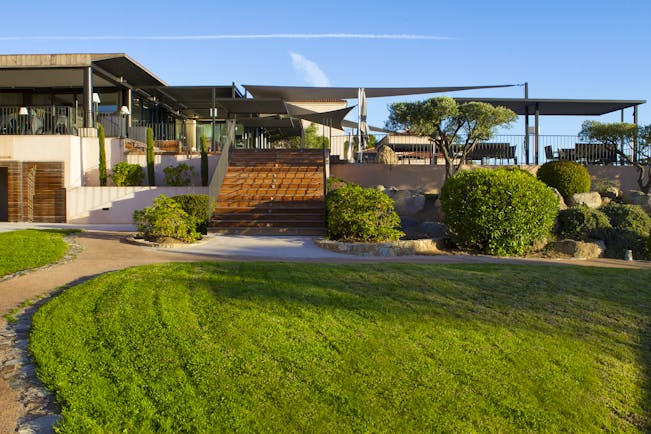 Gardens with green grassy lawn, bushes and steps leading up to a patio area