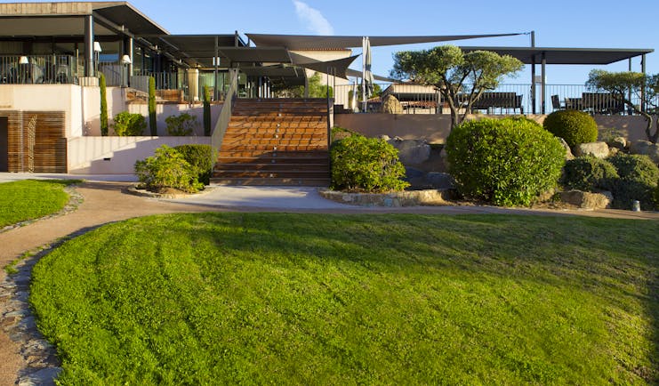 Gardens with green grassy lawn, bushes and steps leading up to a patio area