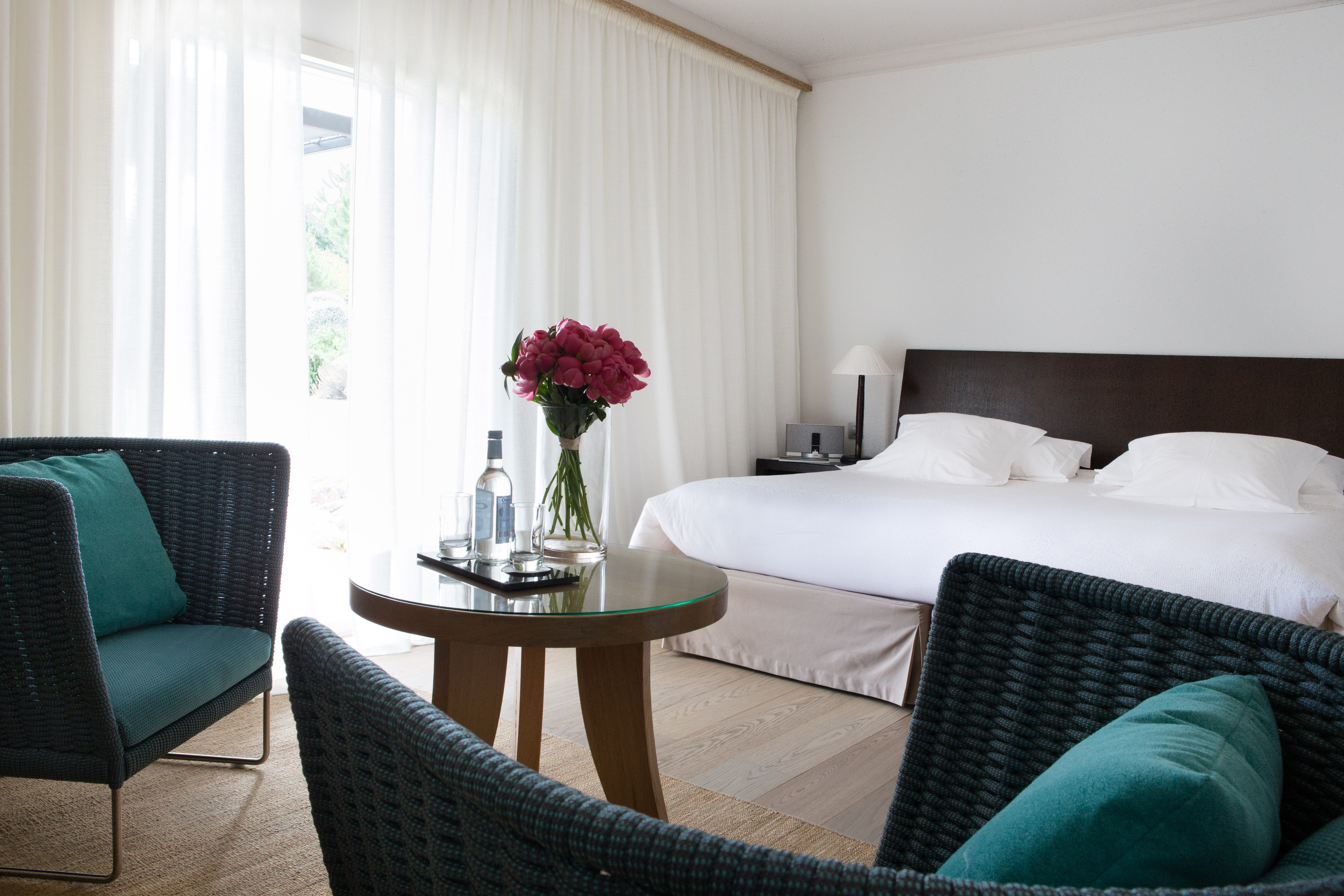 Guest room with double bed, arm chairs and white draping curtains 