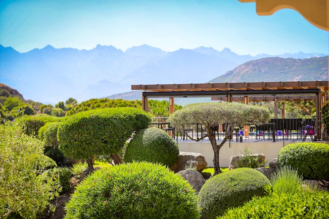 View of terrace amongst the gardens with hedges and trees in front and mountains in background
