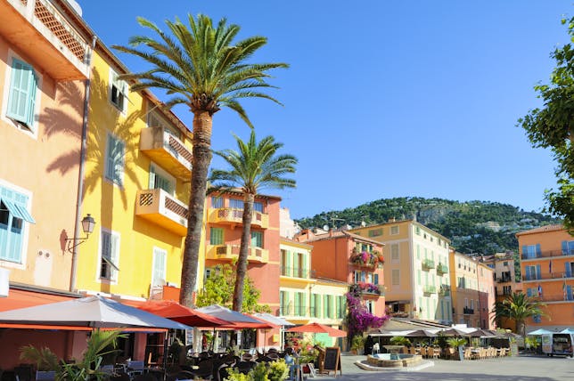 Pink and yellow houses with palmtrees lining a square in Villefranche sur Mer
