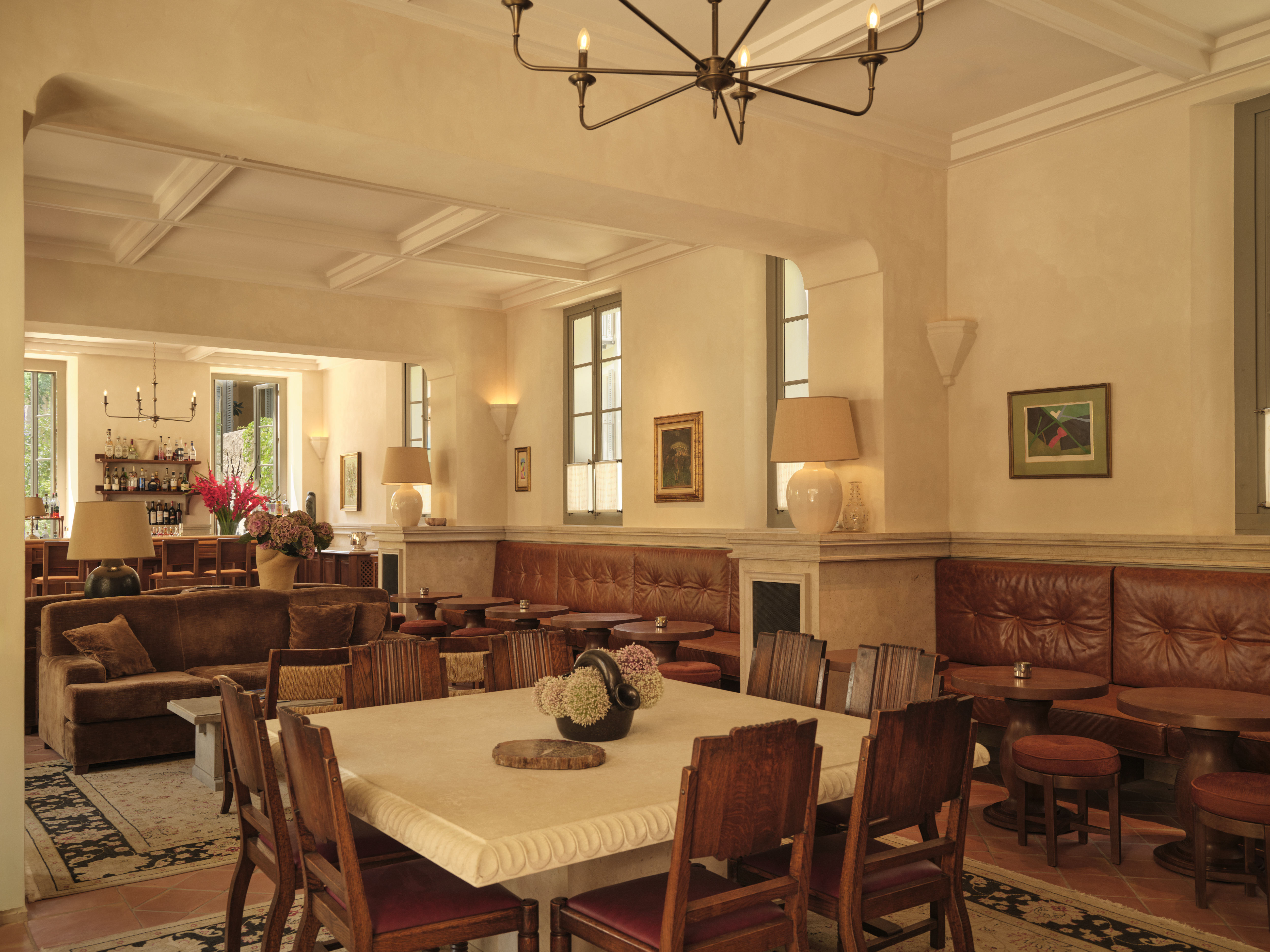 Hotel du Couvent bar with brown leather sofas, small wooden tables and stools, and larger square stone tables in the centre of the room, with bright windows on the exterior walls