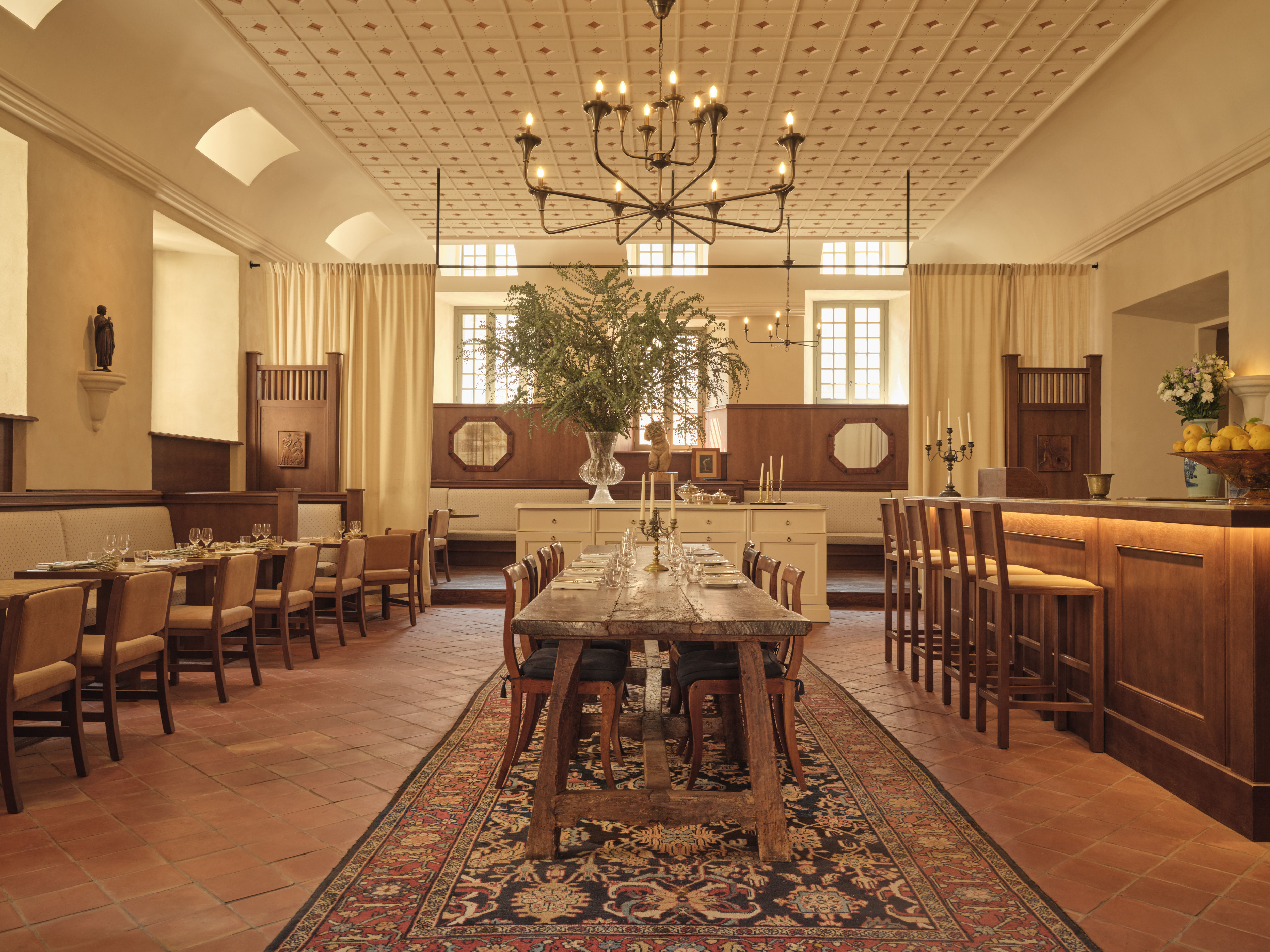 Hotel du Couvent Le Bistrot des Serruriers with ornate rug on terracotta tiles, elegant chandelier, and classically wooden chairs and tables, with a bar on the right side