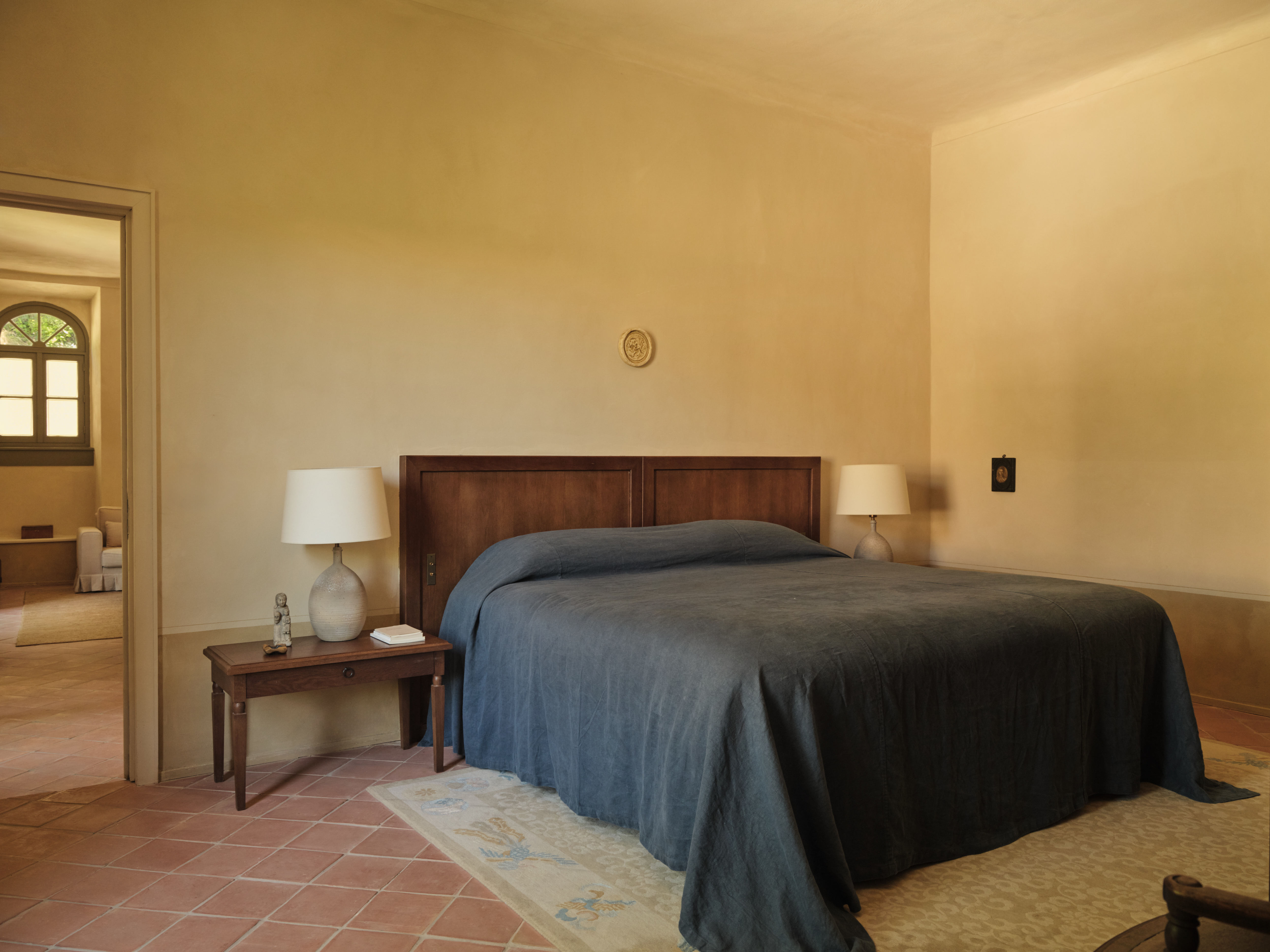Hotel du Couvent double bedroom with blue bed linen, a simplistic dark wood headboard, warm, minimalist aesthetic, and terracotta floor tiles