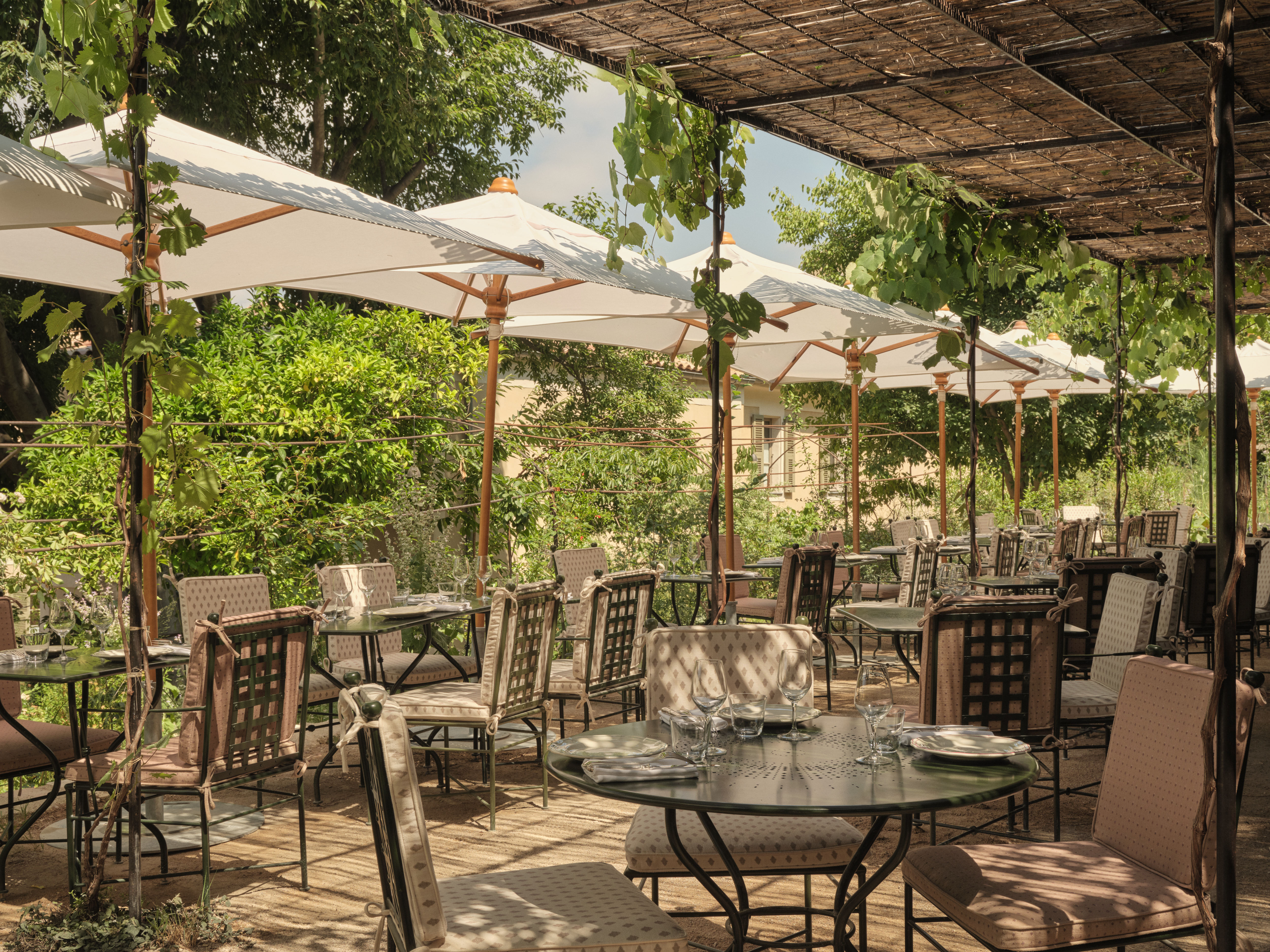Hotel du Couvent La Guinguette, with wrought iron chairs and tables under parasols, trees, and winding vines