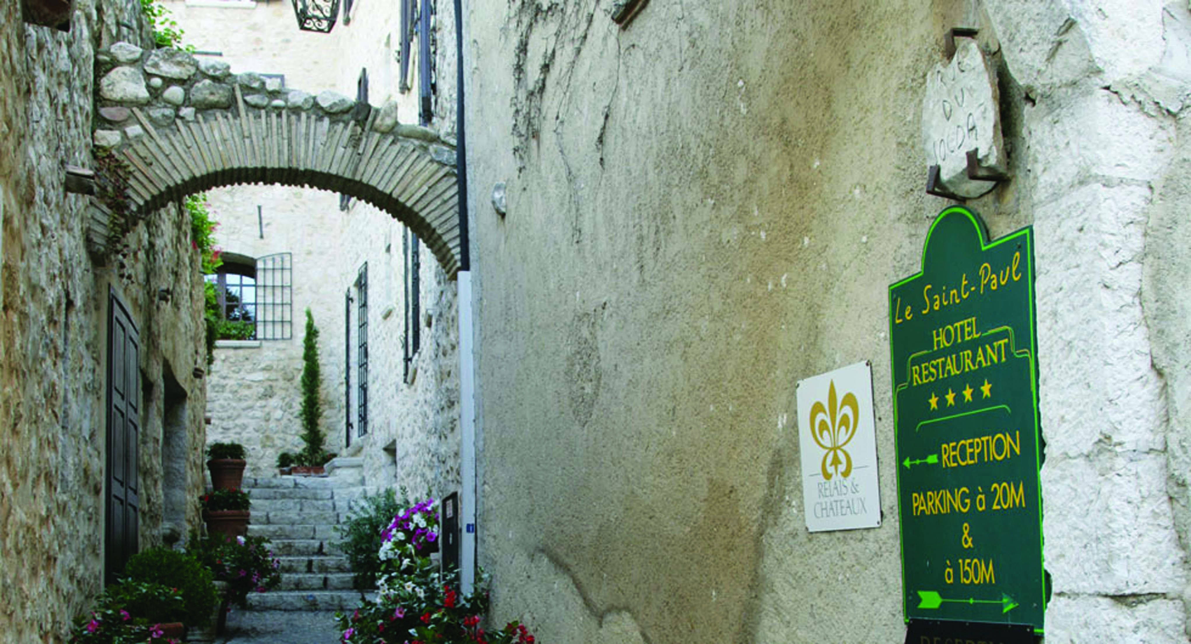 Le Saint Paul Cote d'Azur main entrance stone building with archway leading down steps and two topiary trees