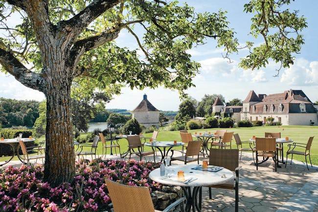Chateau des Vigiers Dordogne brasserie chai dining area next to a tree and flower bed with pink flowers