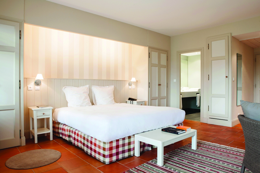 Chateau des Vigiers Dordogne relais superior bedroom with cream wooden panelled walls and a view to a bathroom