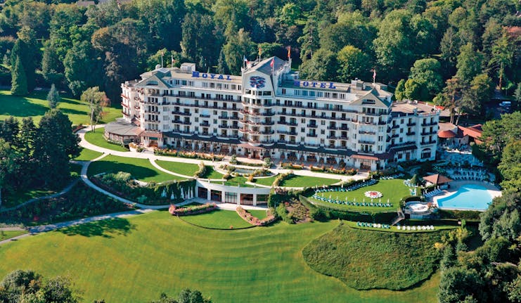 Exterior view of hotel with lawn in front, a pool within its grounds and lots of trees behind 