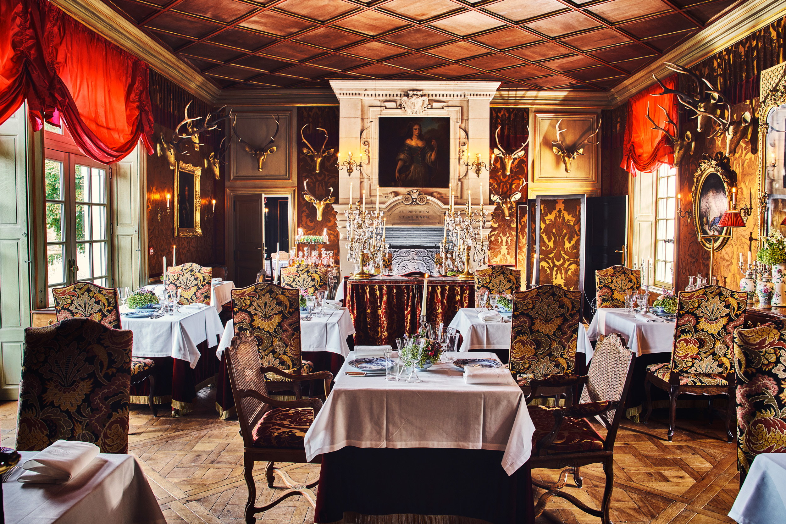 Chateau Louise de la Valliere Restaurant with opulent decor in rich reds and gold, with ornate tables and chairs, and a fireplace