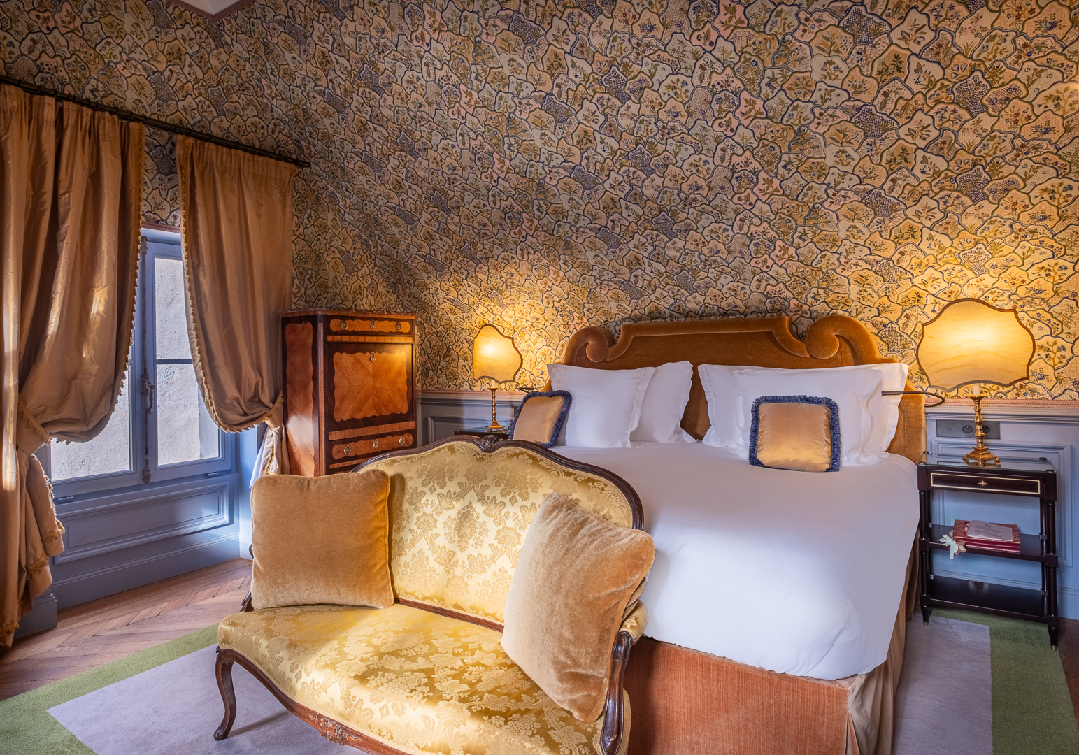 Chateau Louise de la Valliere room with ornate patterned gold wallpaper, sumptuous hardwood furnishings, and draped windows