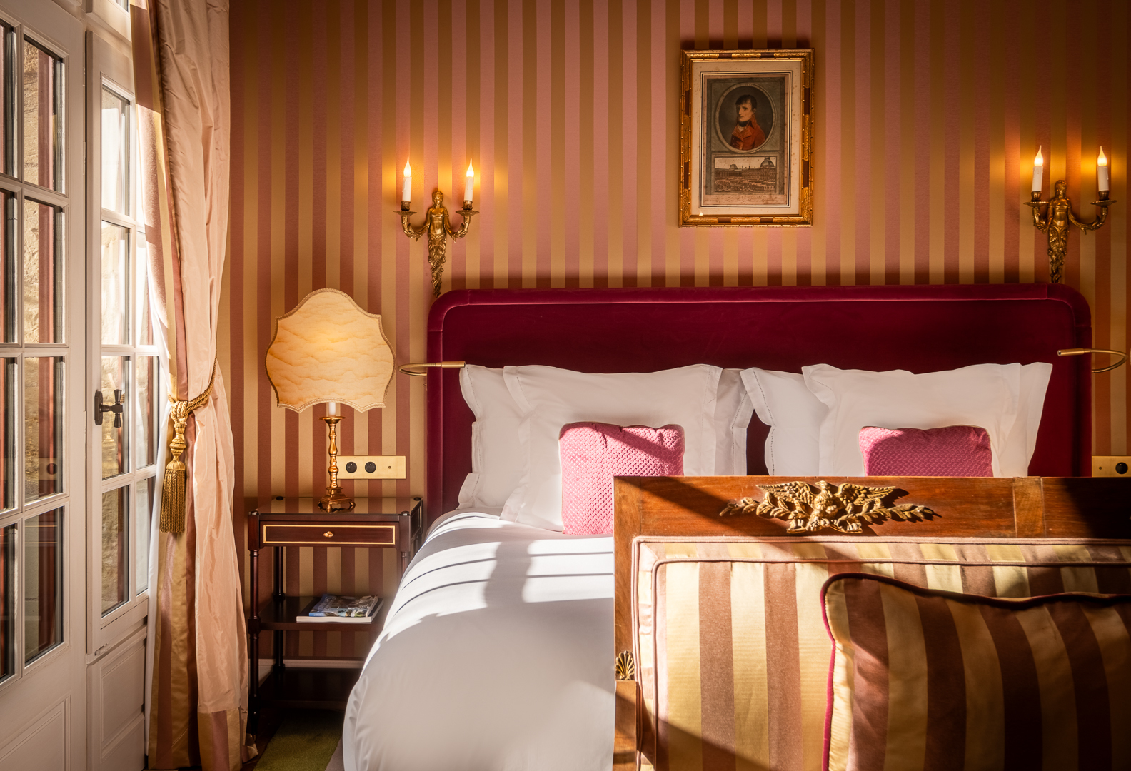 Chateau Louise de la Valliere room with striped gold and peach wallpaper, rich pink velvet headboard, and ornate antique furnishings