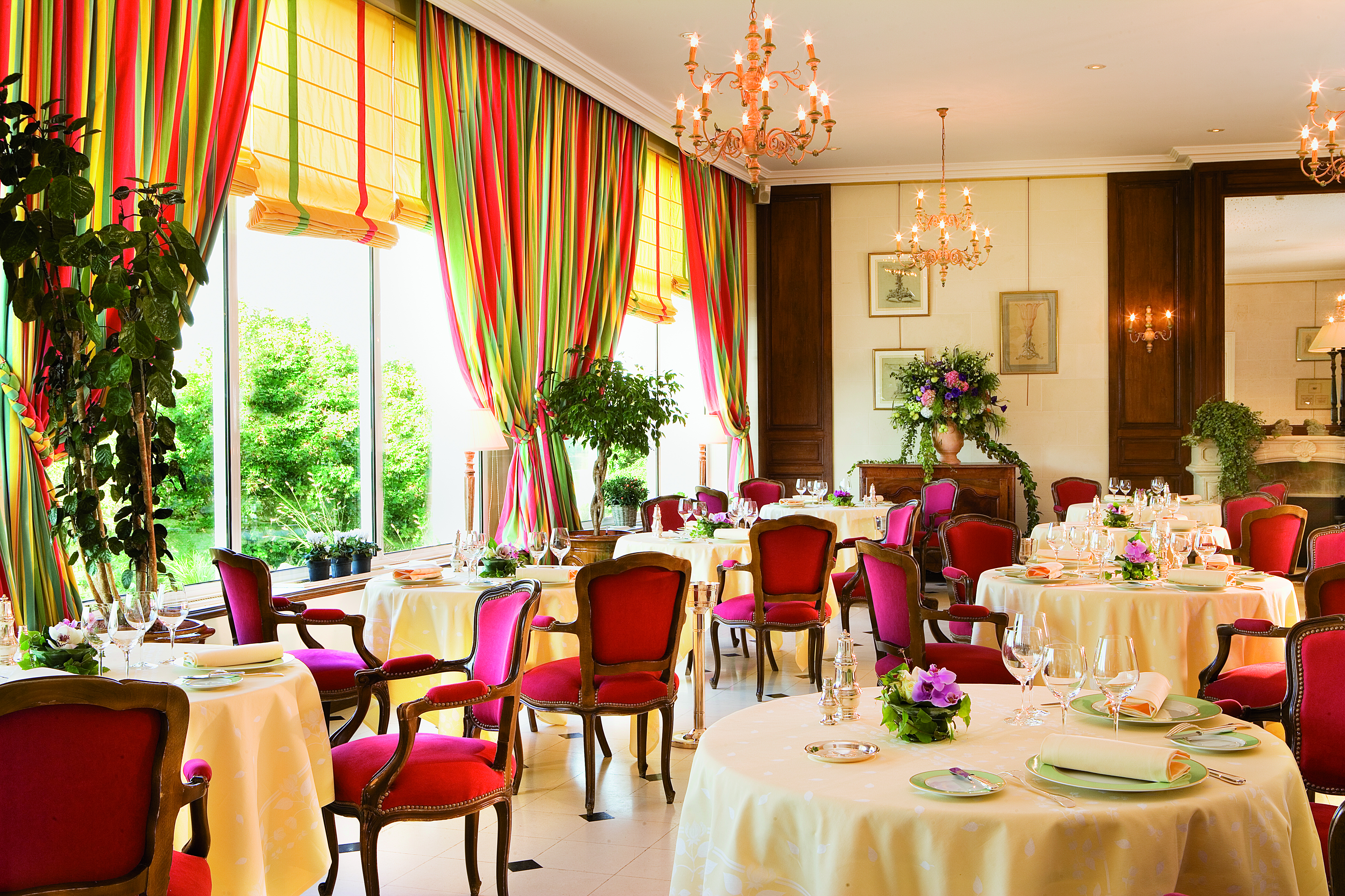 Le Choiseul restaurant with red dining chairs, white circular tables laid out and chandeliers hanging from the ceiling