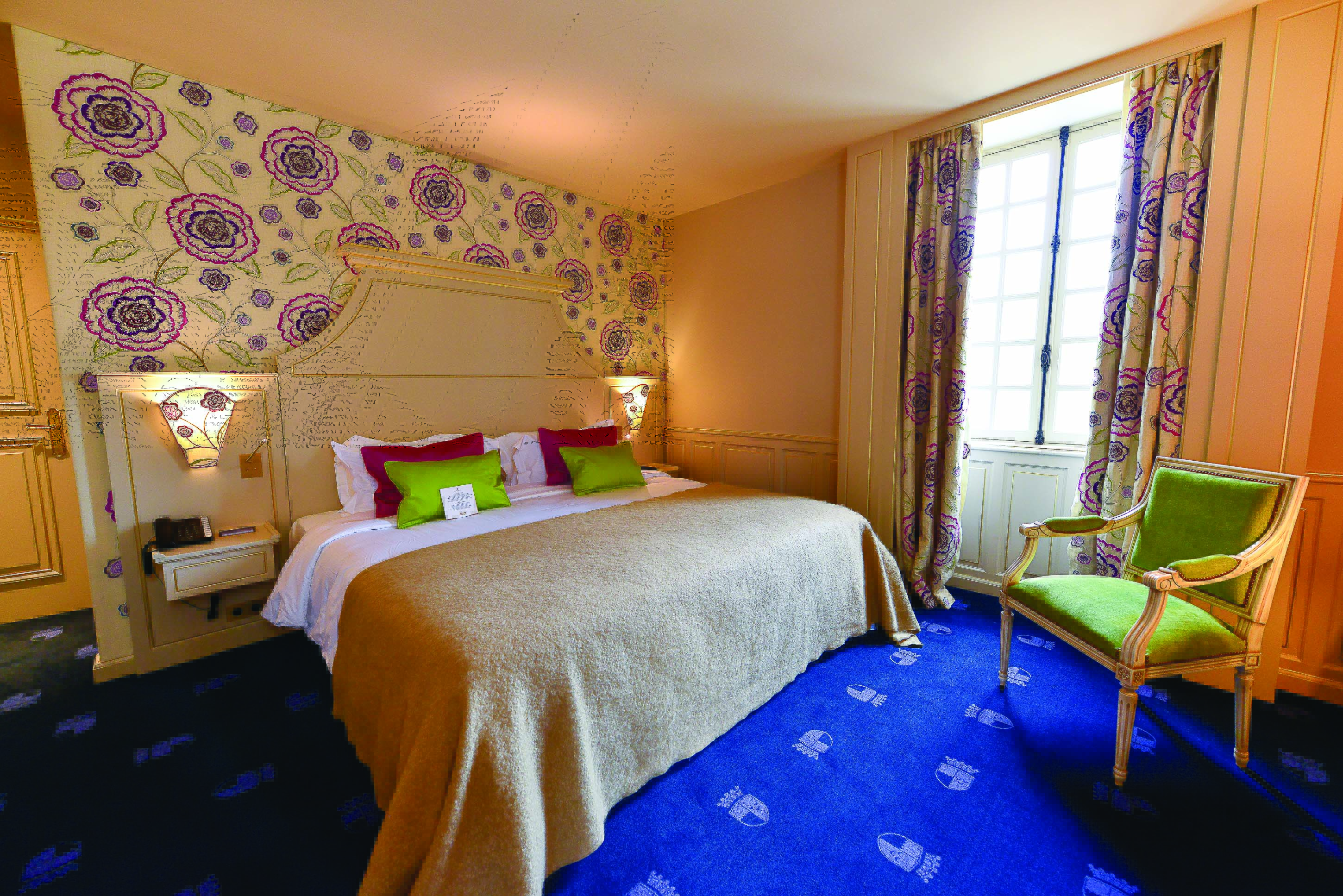 Another bedroom at the Chateau d'Audrieu with blue carpets, a large double bed, and armchair