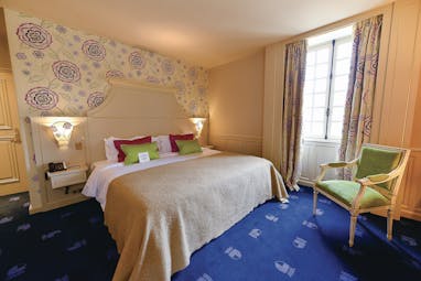 Another bedroom at the Chateau d'Audrieu with blue carpets, a large double bed, and armchair