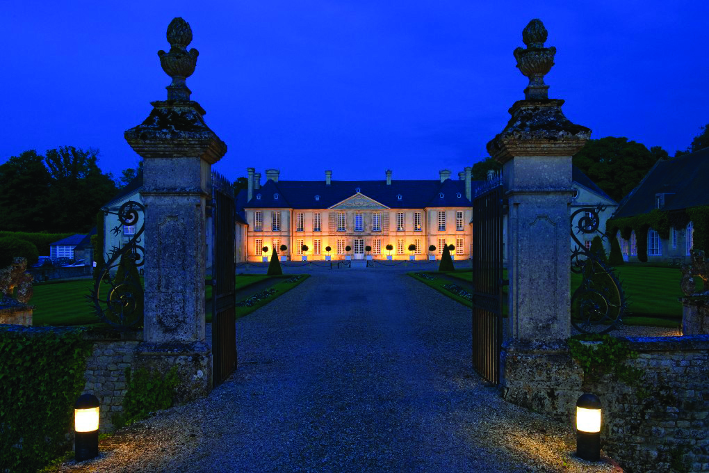 Entrance to the hotel through open gates at night time with the hotel dimly lit with orange lights 