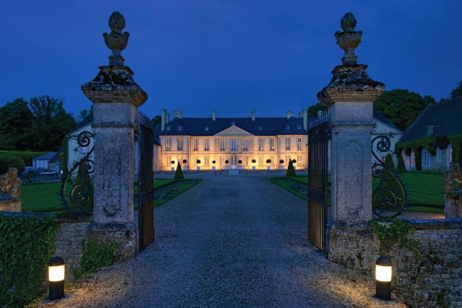 Entrance to the hotel through open gates at night time with the hotel dimly lit with orange lights 