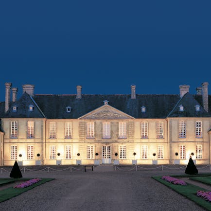 Exterior of the Chateau d'Audrieu, shows big white hotel building lit up with yellow lights 