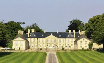 Exterior of Chateau d'Audrieu with a mown lawn in front of the big white hotel building