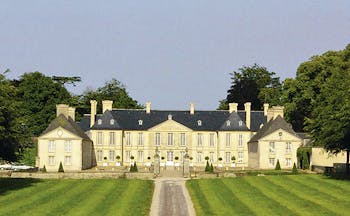 Exterior of Chateau d'Audrieu with a mown lawn in front of the big white hotel building