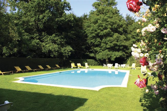 View of the outdoor swimming pool with red and white roses on vines and white deckchairs surrounidng the pool