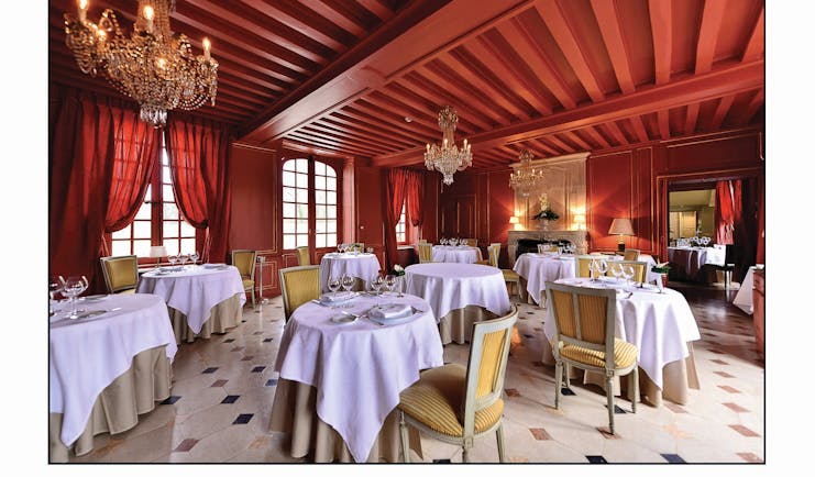 Chateau d'Audrieu dining area with red ceilings and walls and dining tables set up around the room 