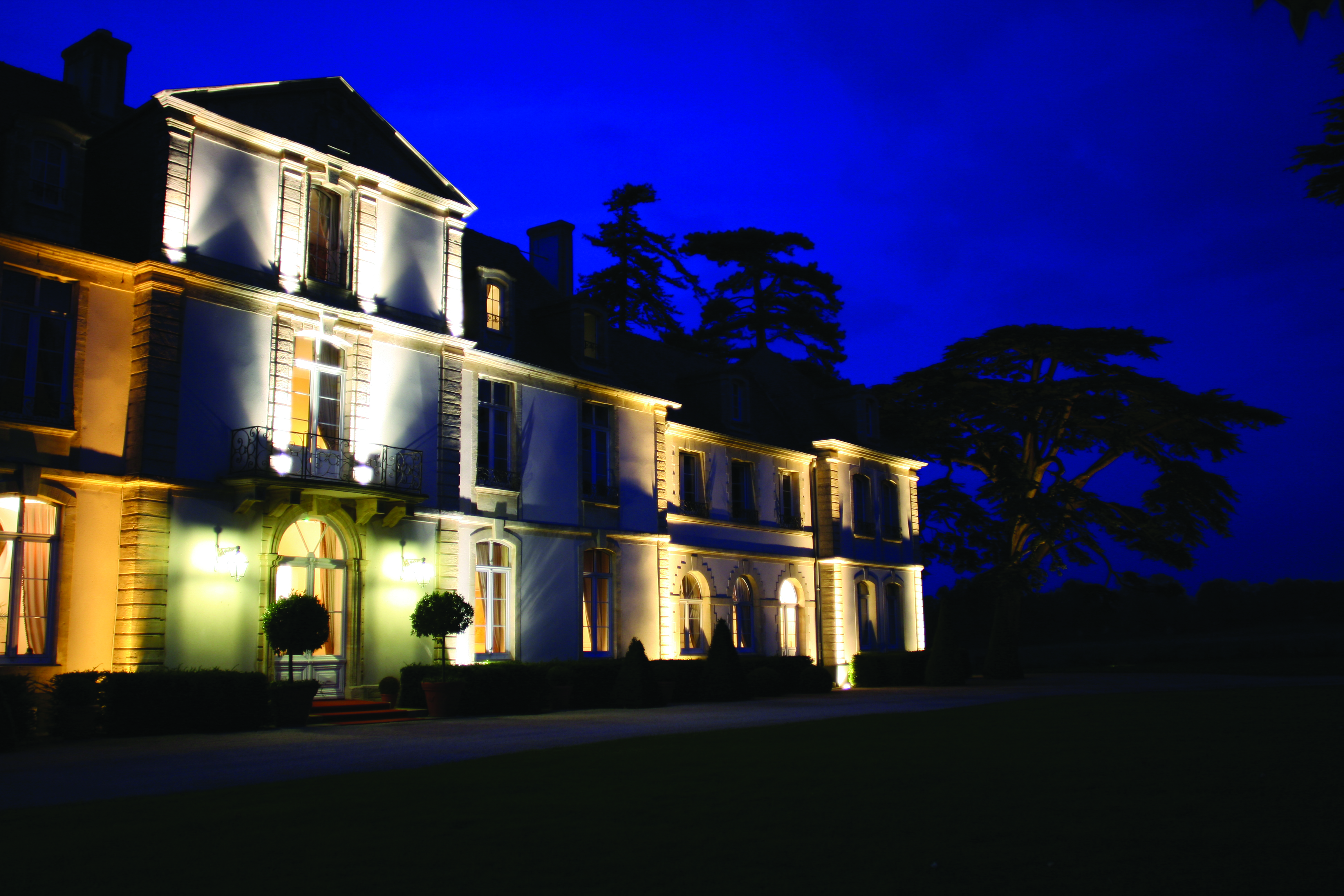 Exterior of hotel at night with a dark sky and the white building lit up by yellow lights 