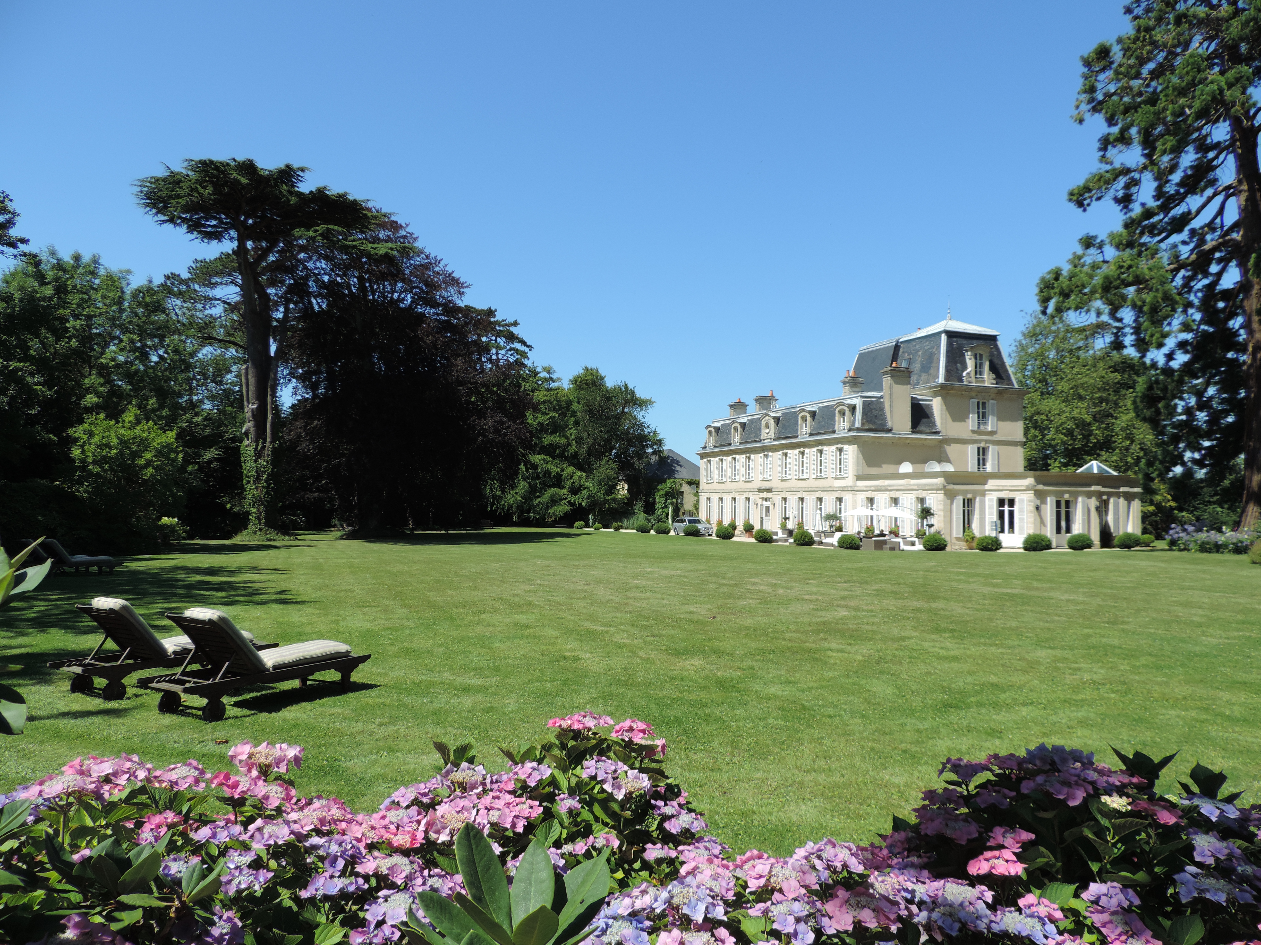 Exterior of hotel and gardens with pink flowers, sun loungers on the lawn and hotel 