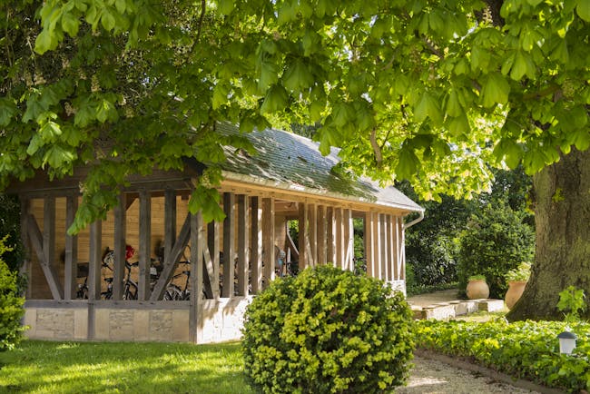 Outdoor stable area with bushes and trees with large wooden stable area with bikes inside