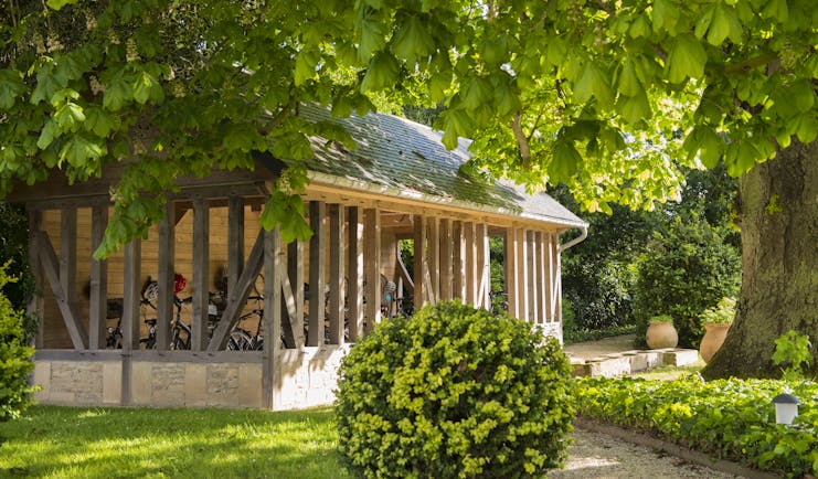 Outdoor stable area with bushes and trees with large wooden stable area with bikes inside