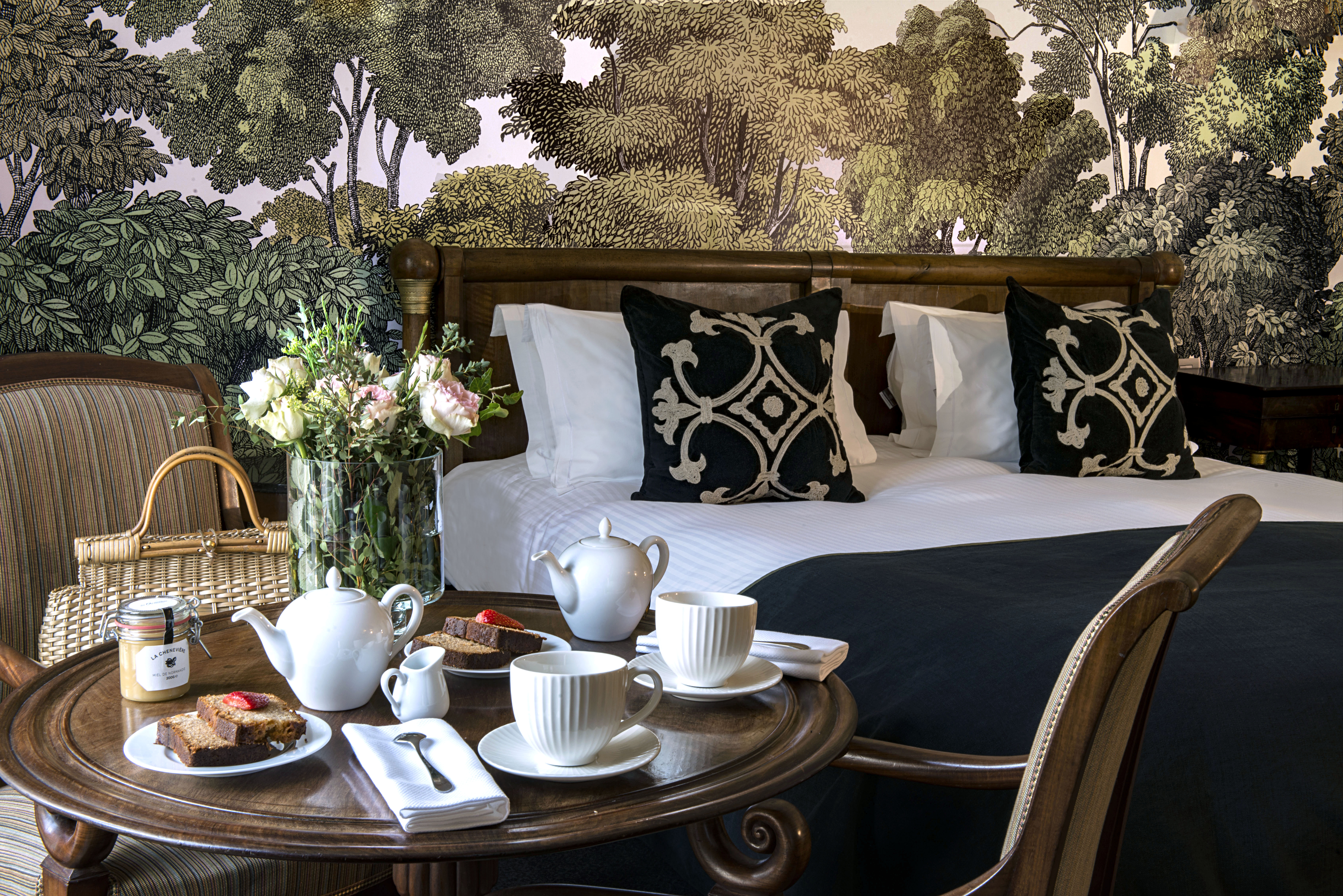 Tea and cake set up on a table in a bedroom with flowers on the table 
