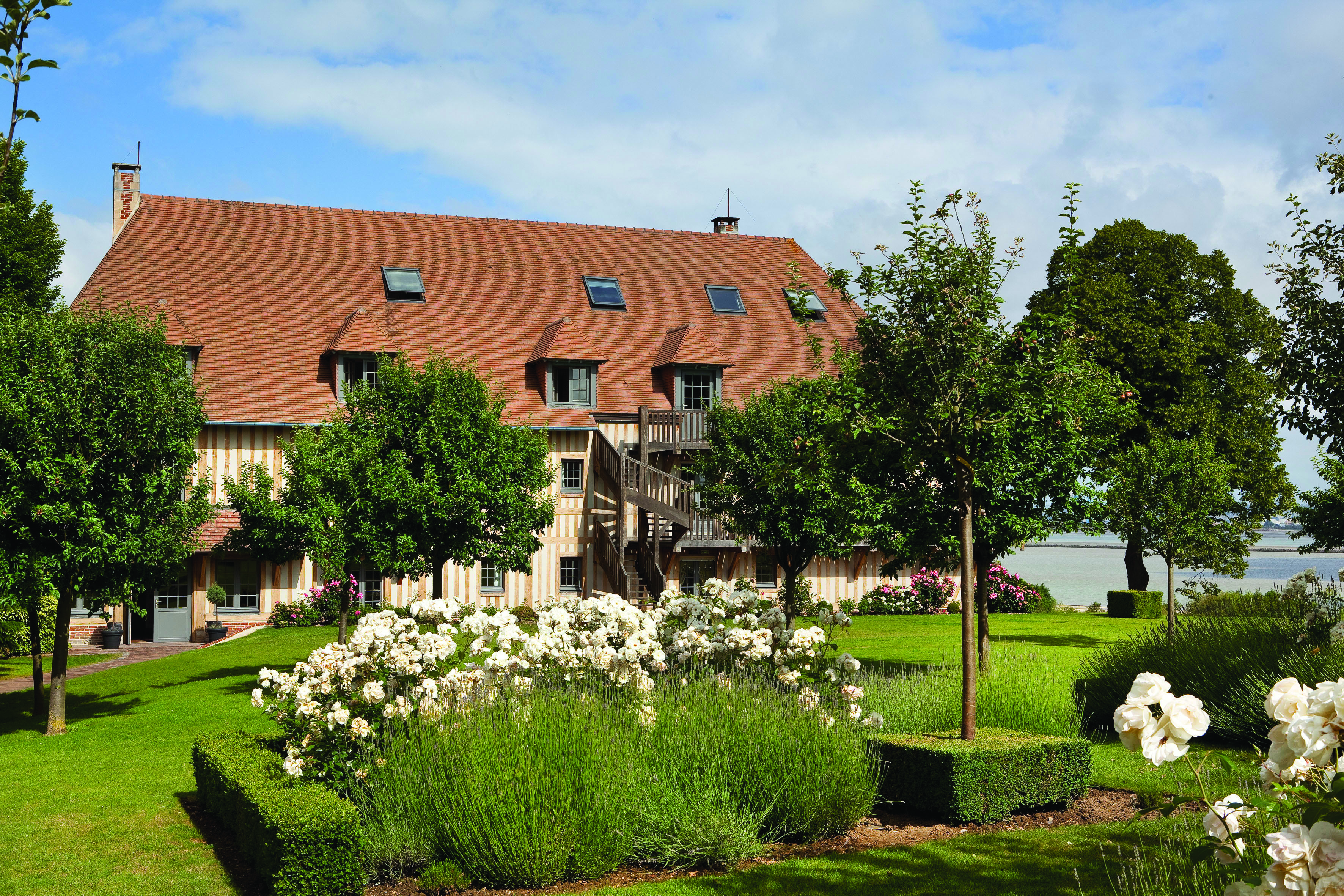 Ferme St Simeon Honfleur house with high red roof and lawns, roses and trees in gardeen